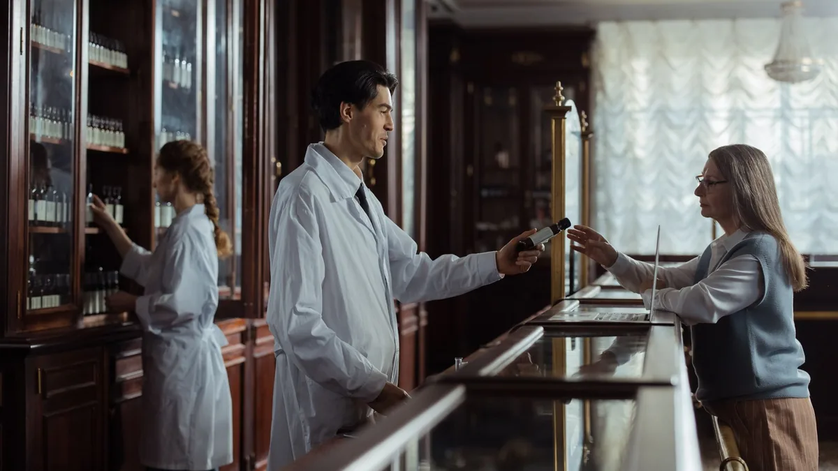A pharmacist hands medication to a customer at a classic vintage pharmacy counter.