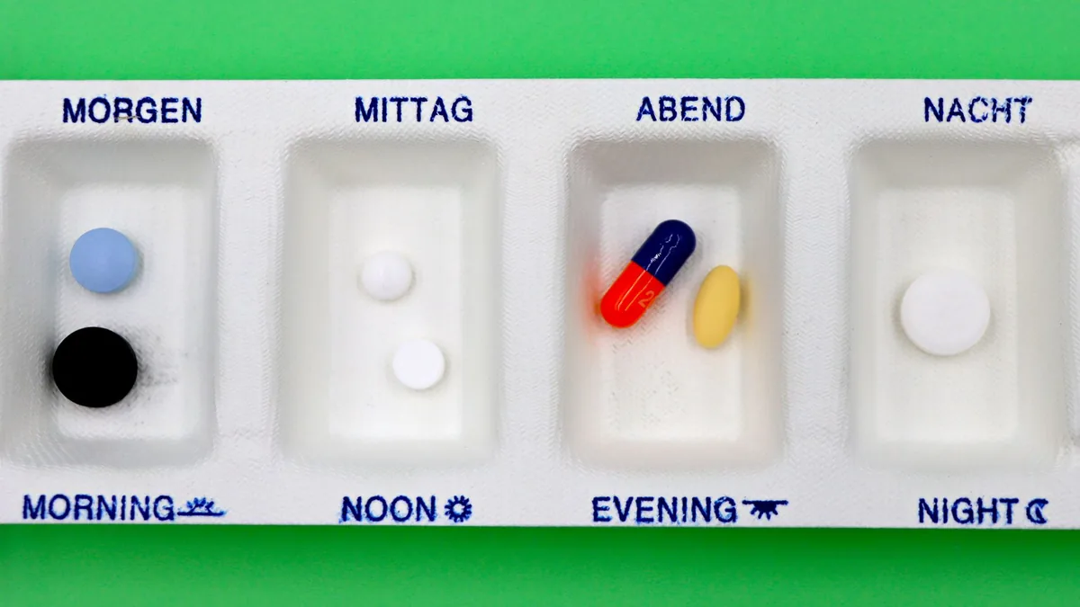 A daily medication organizer with pills for different times, set against a green backdrop.
